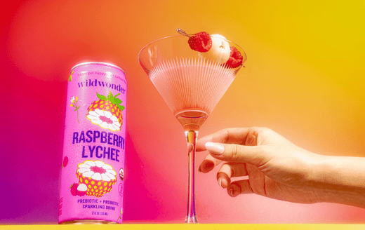 Raspberry Lychee martini mocktail in martini glass garnished with raspberries and lychees next to a can of wildwonder