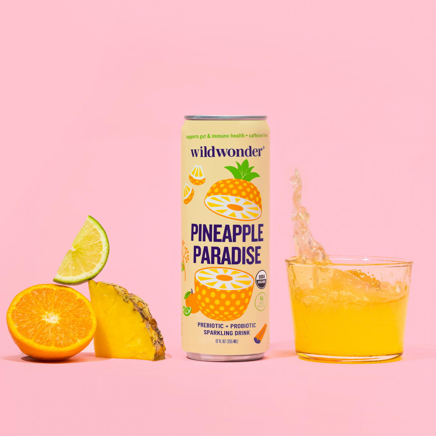 A can of wildwonder's Pineapple Paradise. A glass of the drink is to the right, while cut fruit pieces of lime, tangerine and pineapple are to the left.