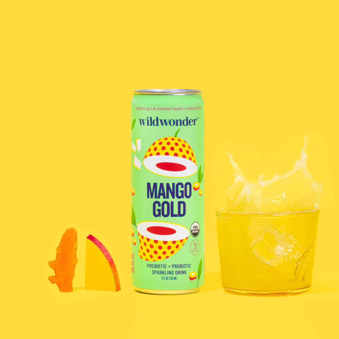 A can of Mango Gold next to a poured glass, with fresh mango and turmeric.