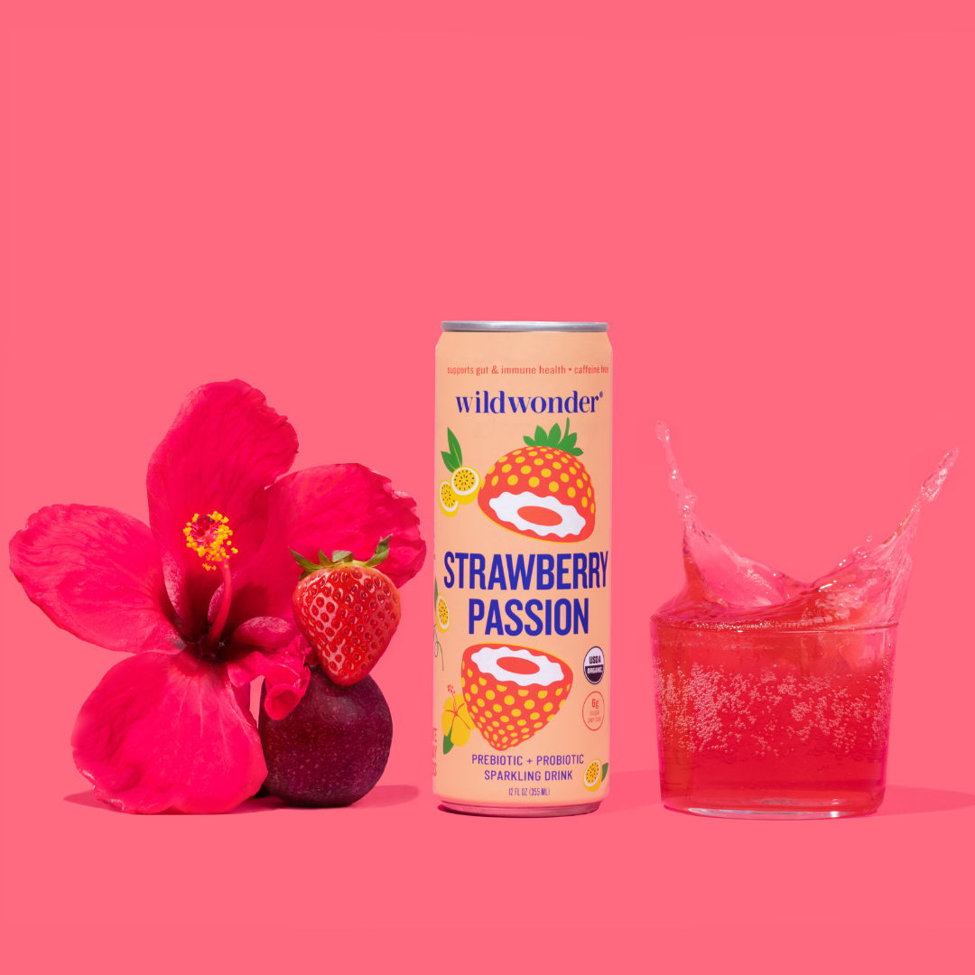 A can of Strawberry Passion next to a poured glass, with a fresh strawberry, passion fruit, and hibiscus flower.